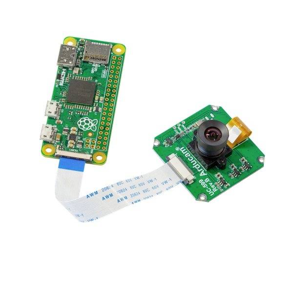 A small, green circuit board with a chip and various ports, connected via a ribbon cable to a camera unit.