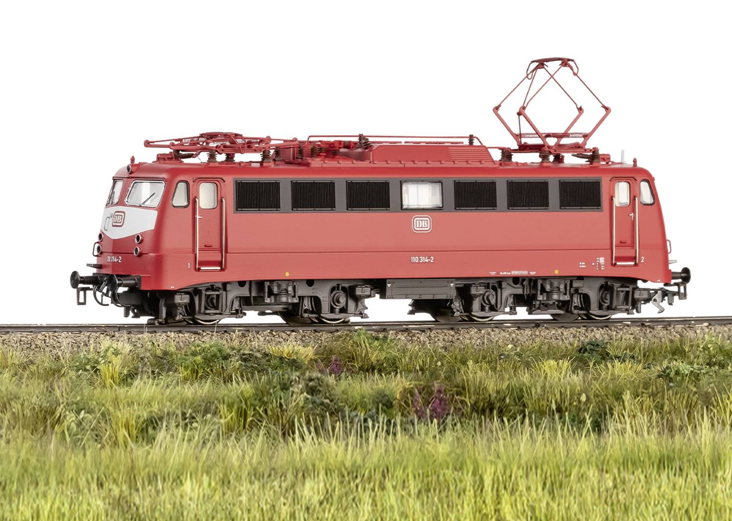 Red electric locomotive on track, side view, against a green meadow landscape. Locomotive number visible.