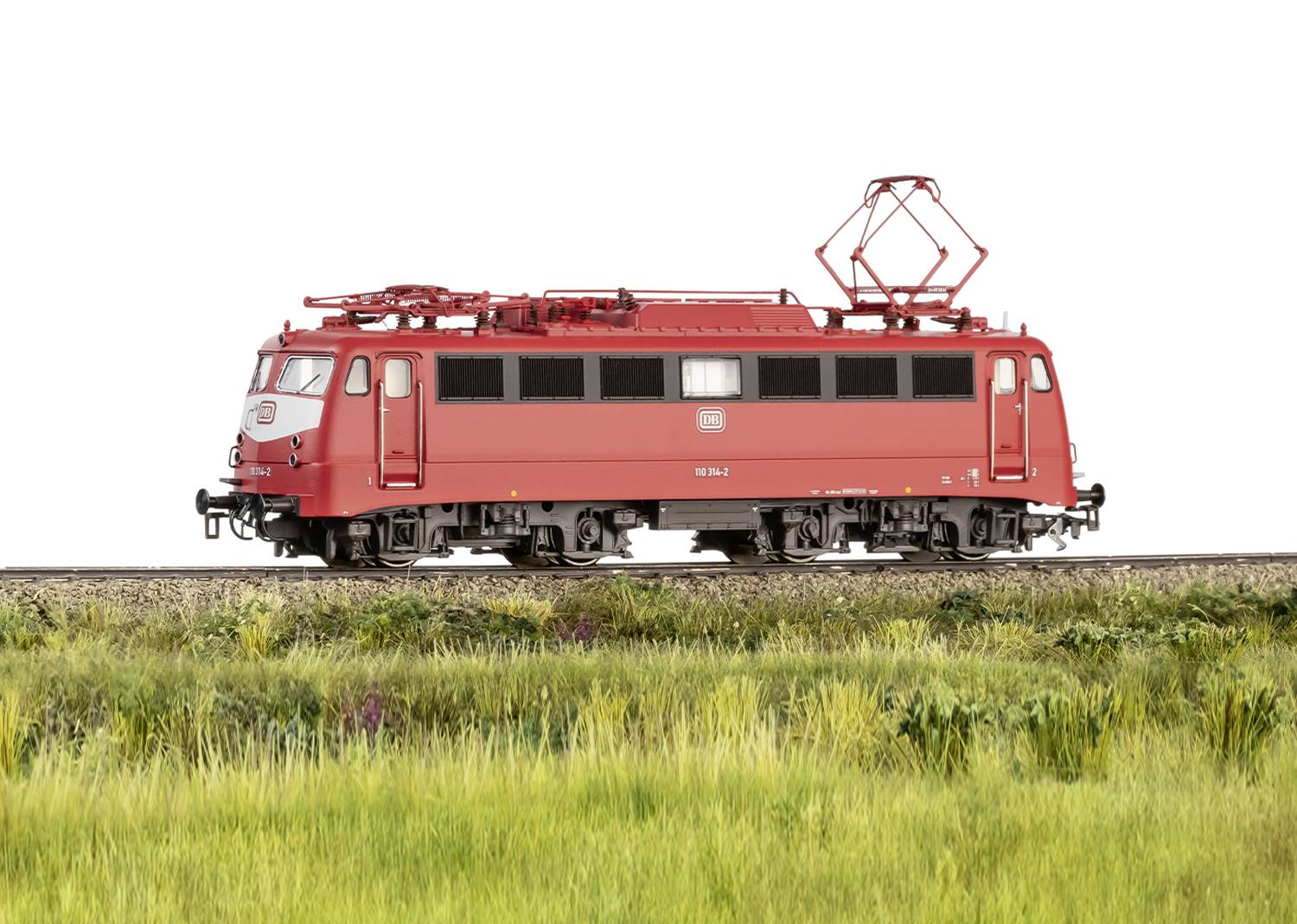 Red electric locomotive on a rail section with green grass in the foreground; side view of the locomotive.
