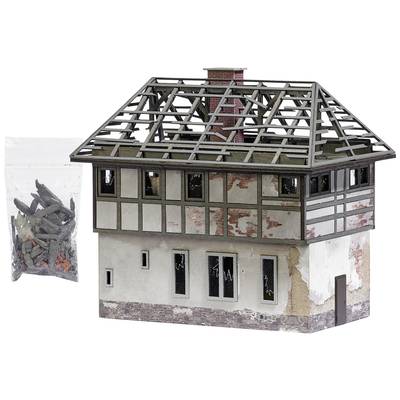 Model of a half-timbered house with visible roof framework, damaged walls and smashed windows. On the left, a bag of accessory parts.