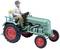 A model tractor with a man at the wheel and a child as a passenger. Both figures are sitting on the green tractor with red wheels.
