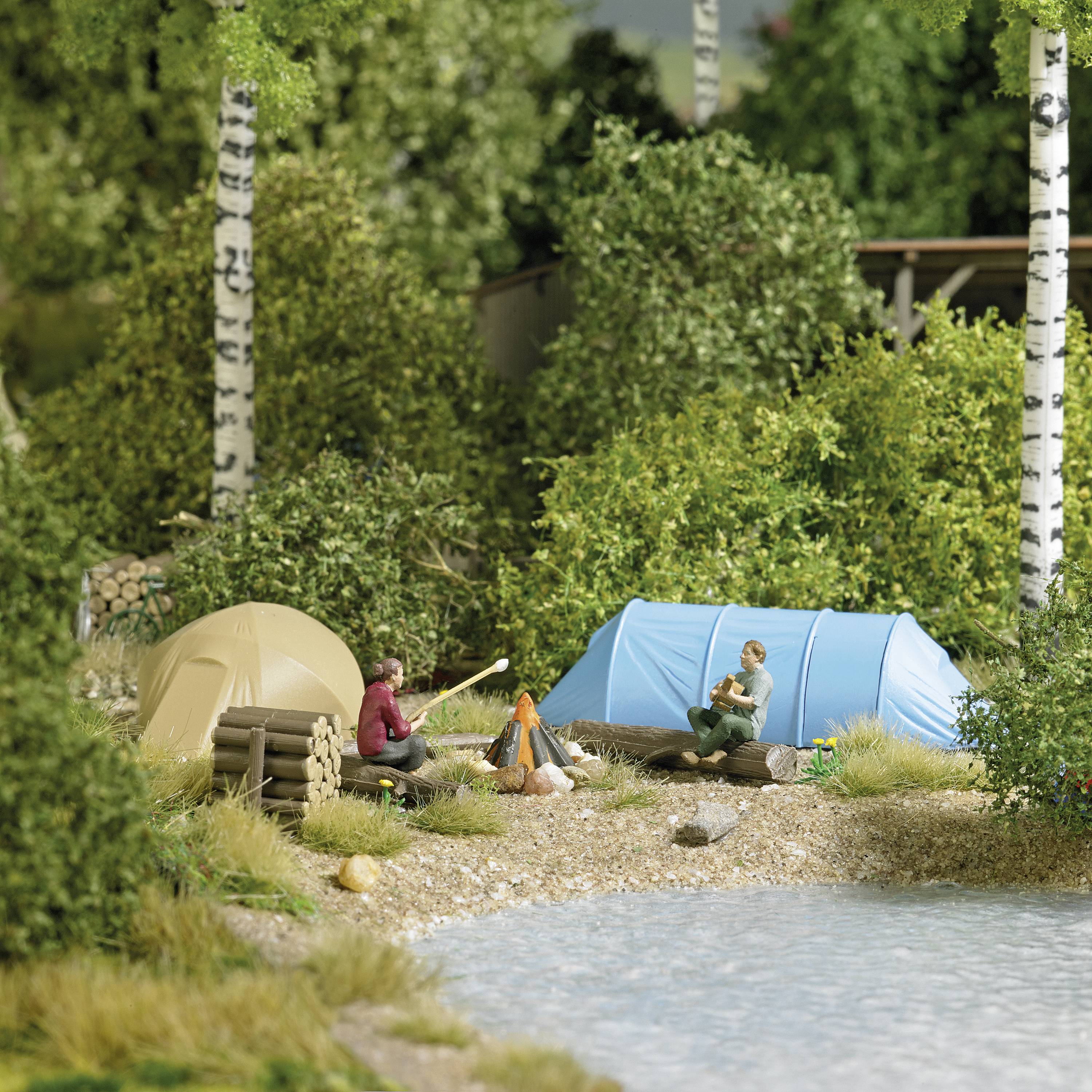Two tents stand by a lake, surrounded by trees. Two people sit on the ground, enjoying nature with a campfire.