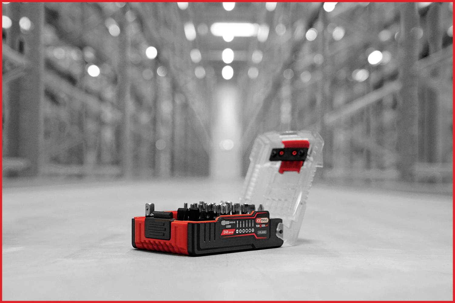 A red bit set in a transparent box lies openly in a blurry warehouse. The focus is on the tools in the foreground.