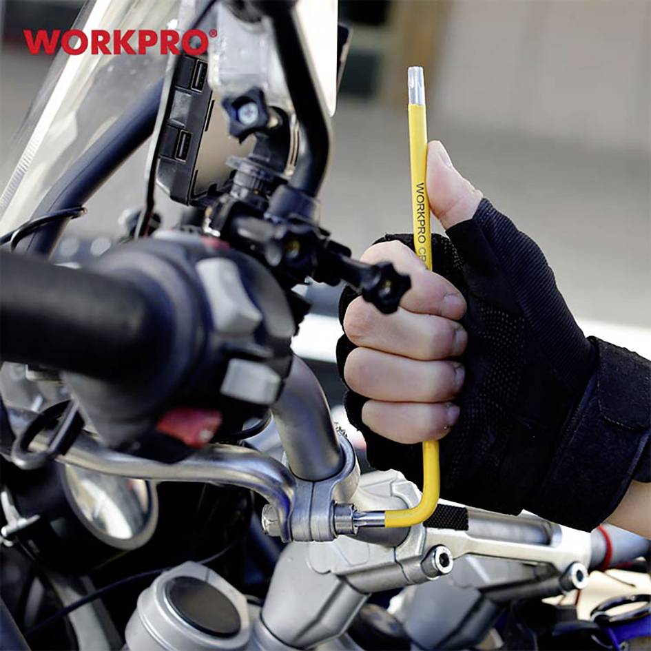 A person wearing gloves is holding a yellow pencil next to a motorcycle handlebar. A blurred cityscape is visible in the background.