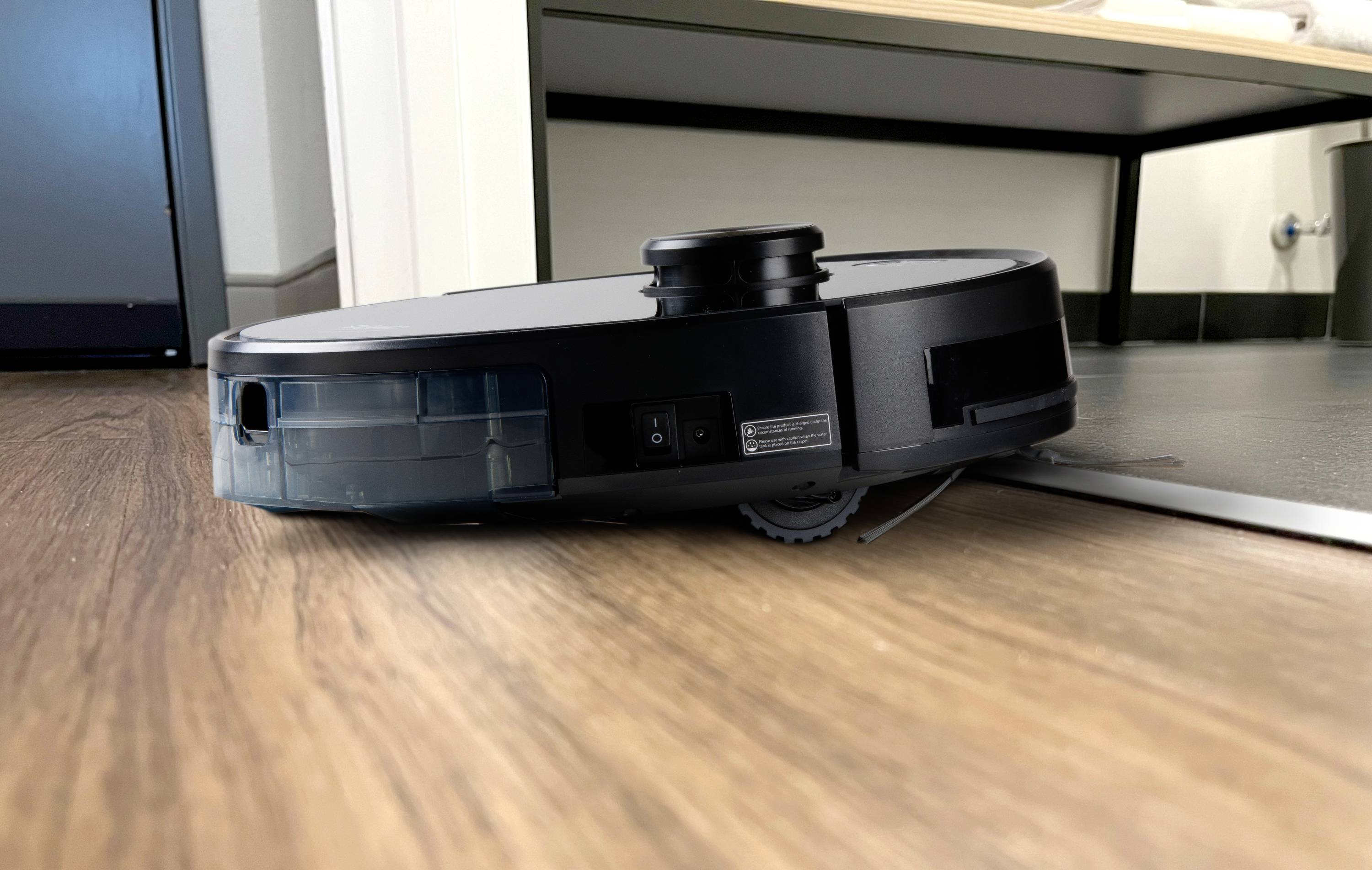 A robot vacuum cleaner moves across a wooden floor and navigates over a small threshold.
