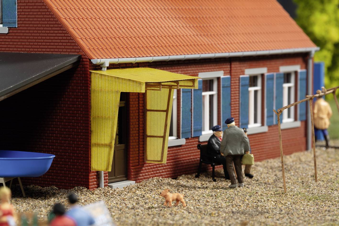 A miniature model shows two people sitting on a bench and conversing in front of a red brick house with blue shutters.