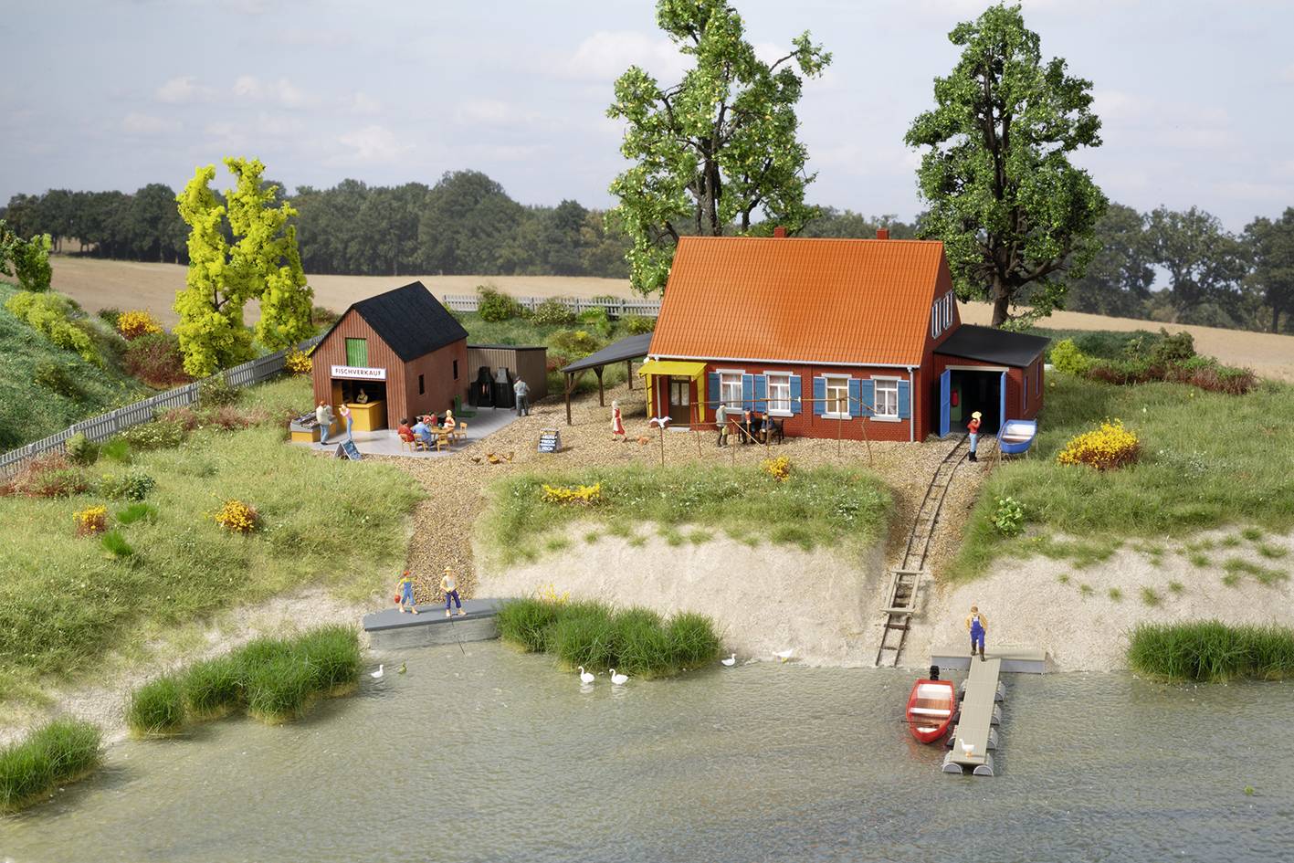 Model landscape with farmhouse: A red house, outbuildings and people on the shore of a lake. Trees and fields in the background.