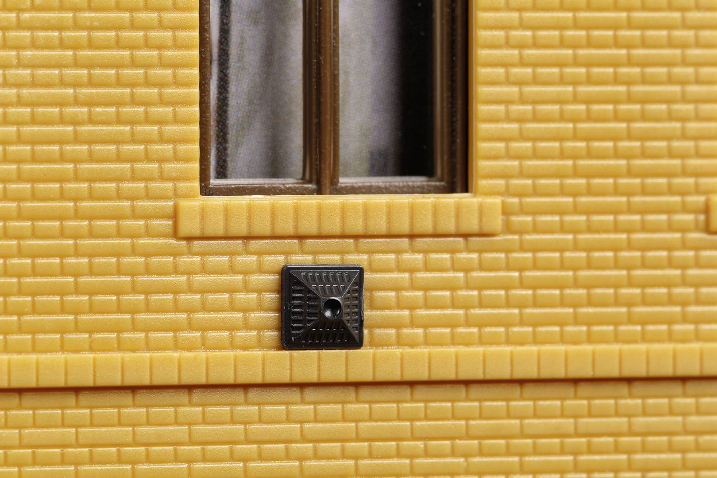 Brick wall with a rectangular window and a black ventilation grille underneath. Building section, focusing on architectural details.