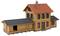 Building model of a two-storey railway station in traditional style with a red roof and wooden cladding. Sign: 'Koppigen'.