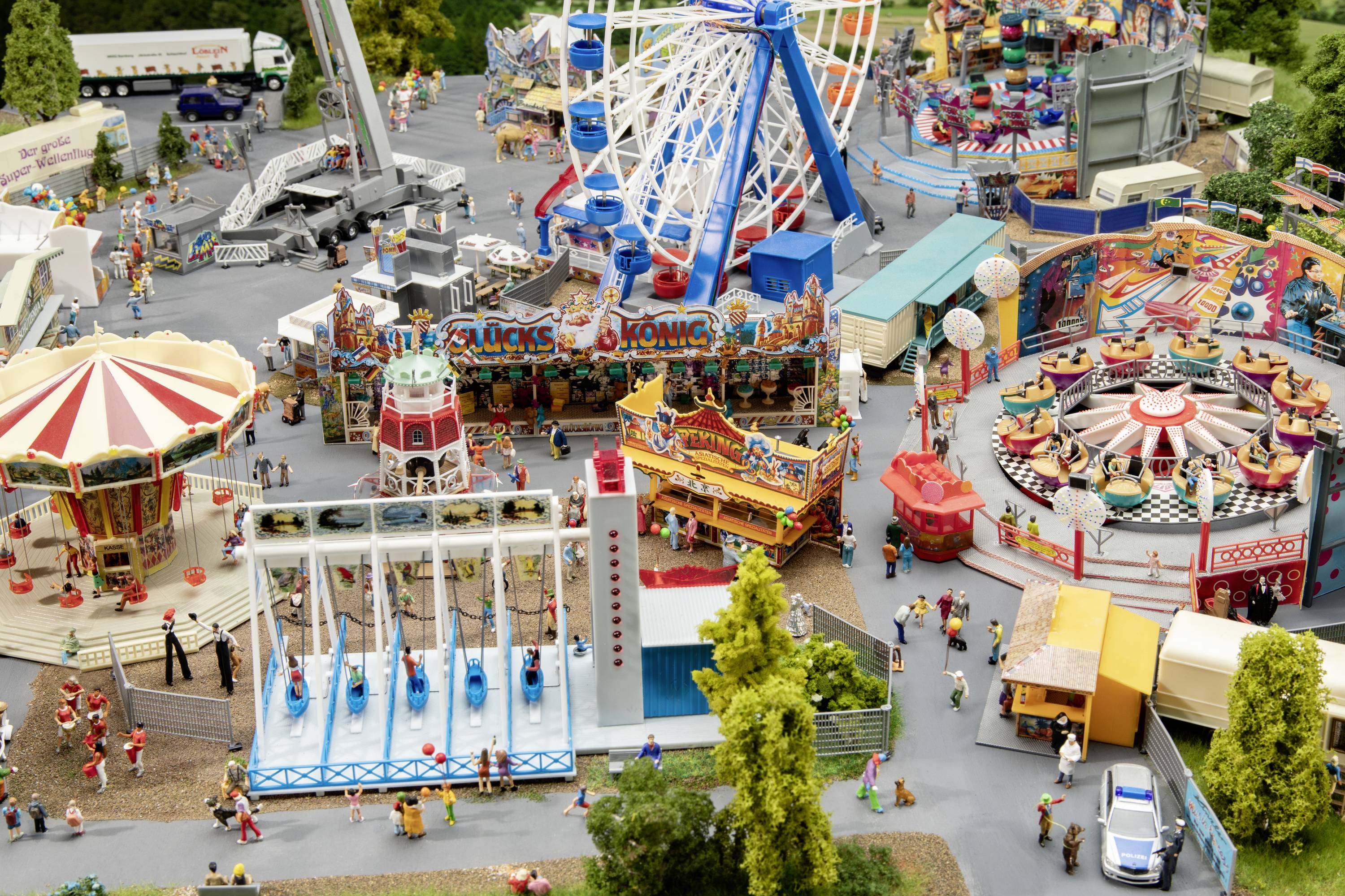 A miniature depiction of a fairground with various rides, crowds of people, and colourful stalls.