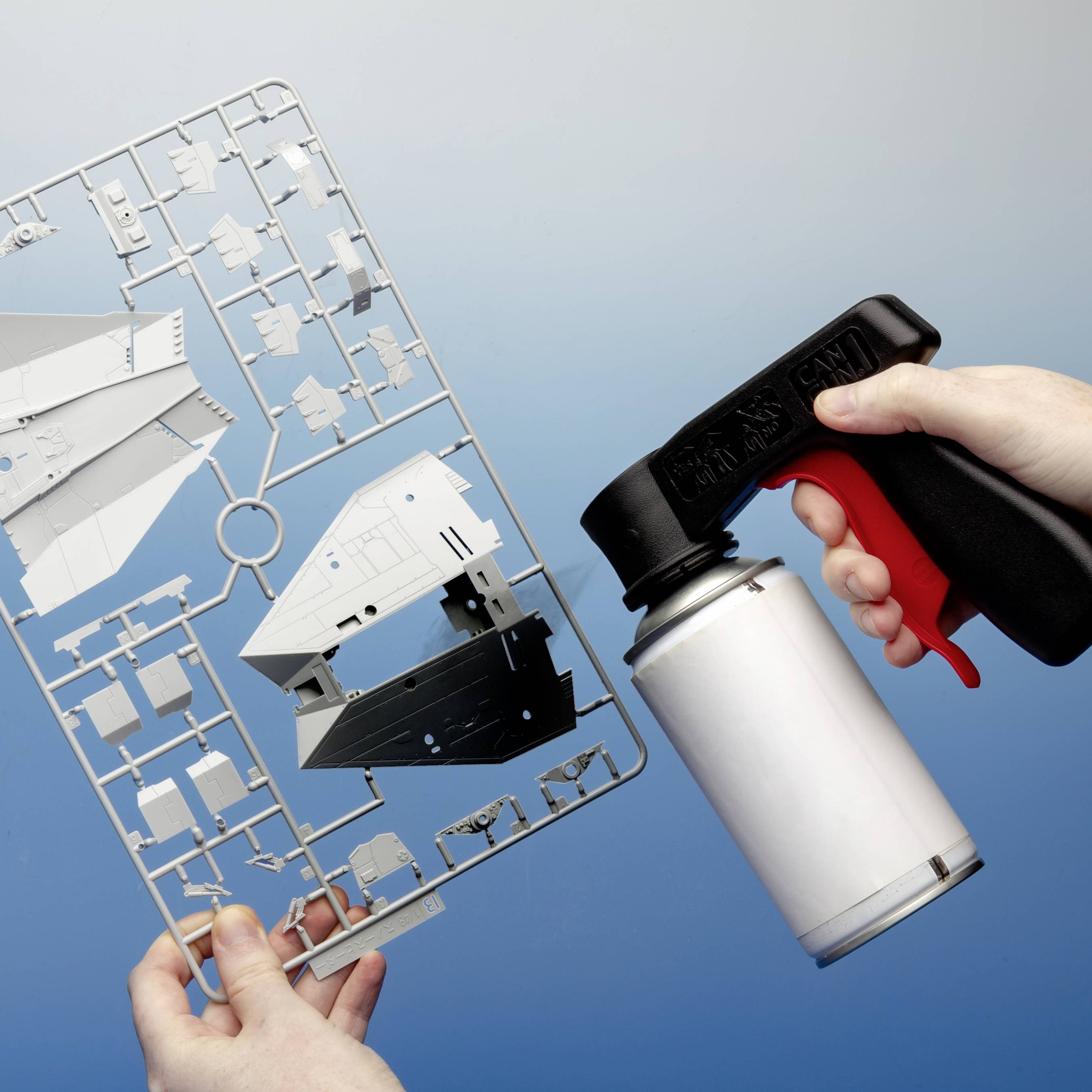 'Model aircraft kit being held in one hand, with an airbrush gun positioned over it by another hand.'