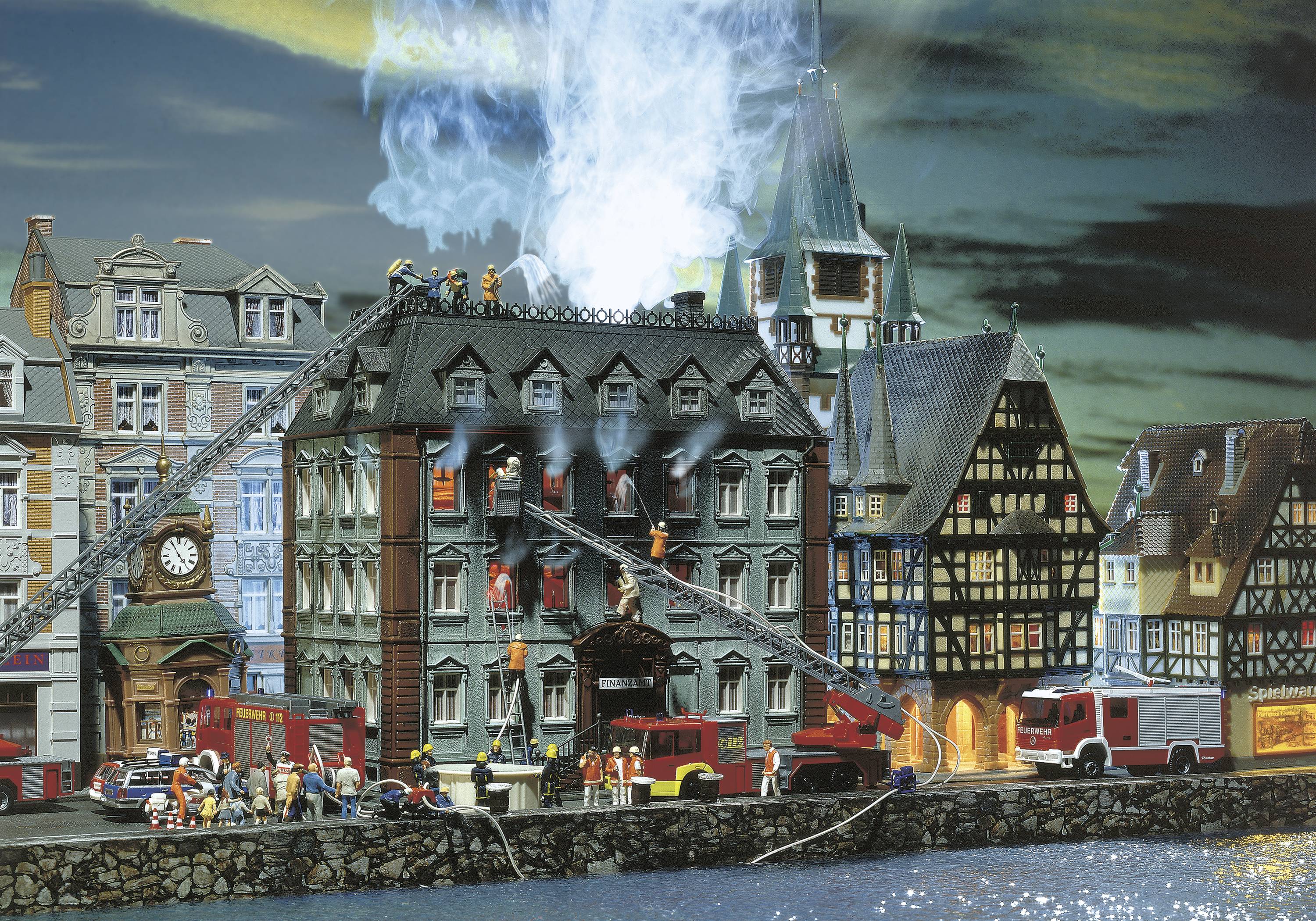 A miniature model of a burning building, surrounded by fire engines and firefighters attempting to extinguish the blaze.