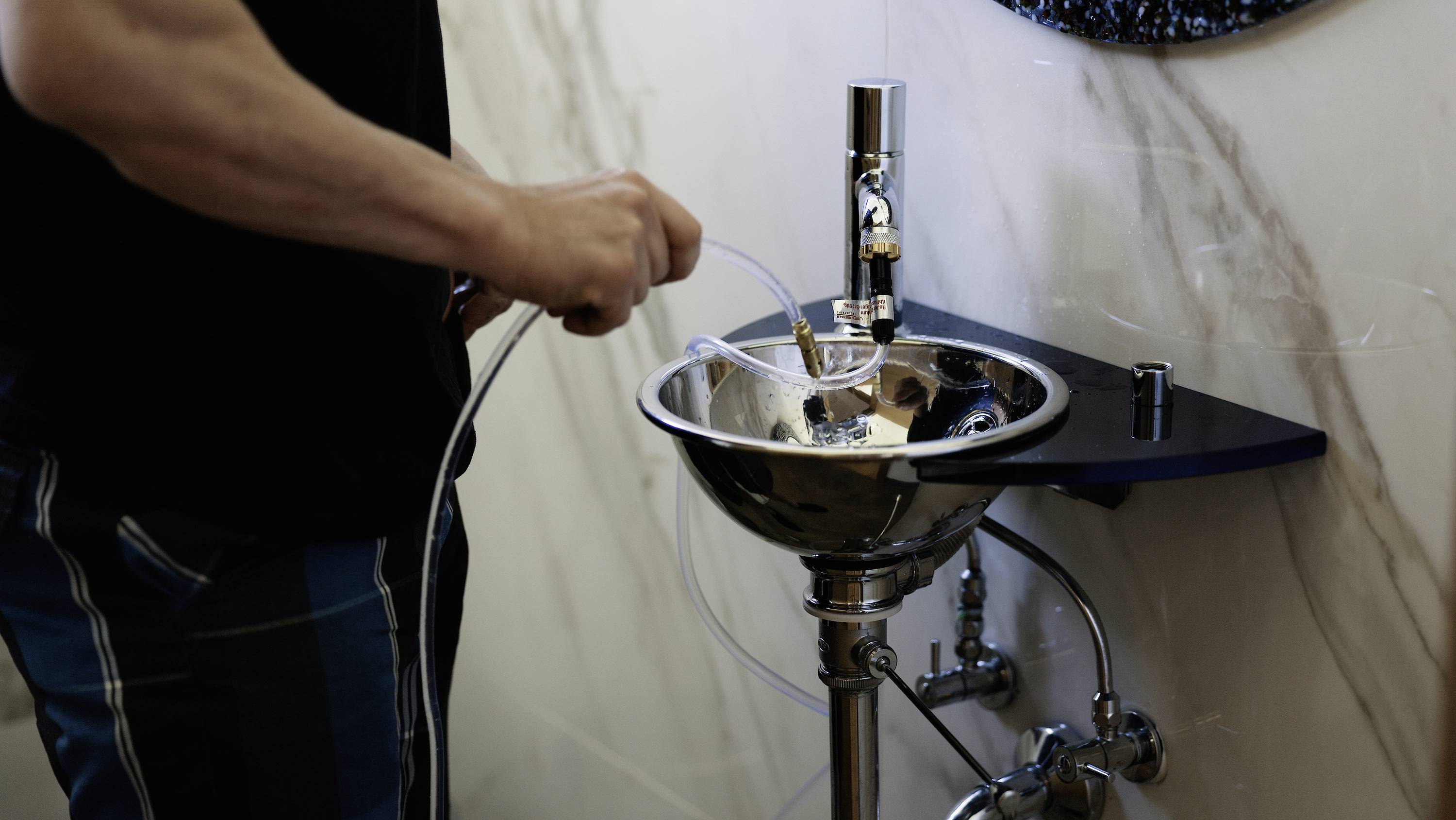 A person is washing a small bowl or device in a metal sink.