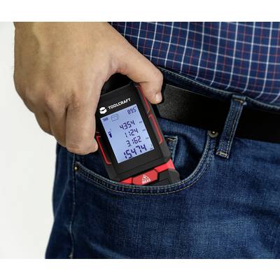 A person slips a digital measuring device with a display into their front trouser pocket. The device shows various measurement readings.