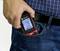 A person slips a digital measuring device with a display into their front trouser pocket. The device shows various measurement readings.