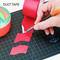 A hand cuts red adhesive tape on a black cutting board. A roll of duct tape is positioned to the left.