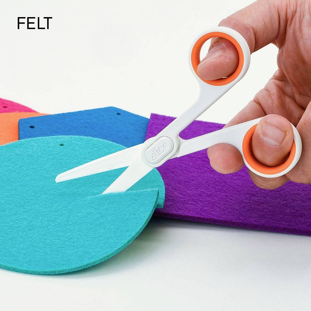 A hand is holding a white scissors with orange handles, cutting a piece of blue felt from several colourful felt pieces.