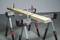 Wooden plank on two metal trestles, secured with clamps.