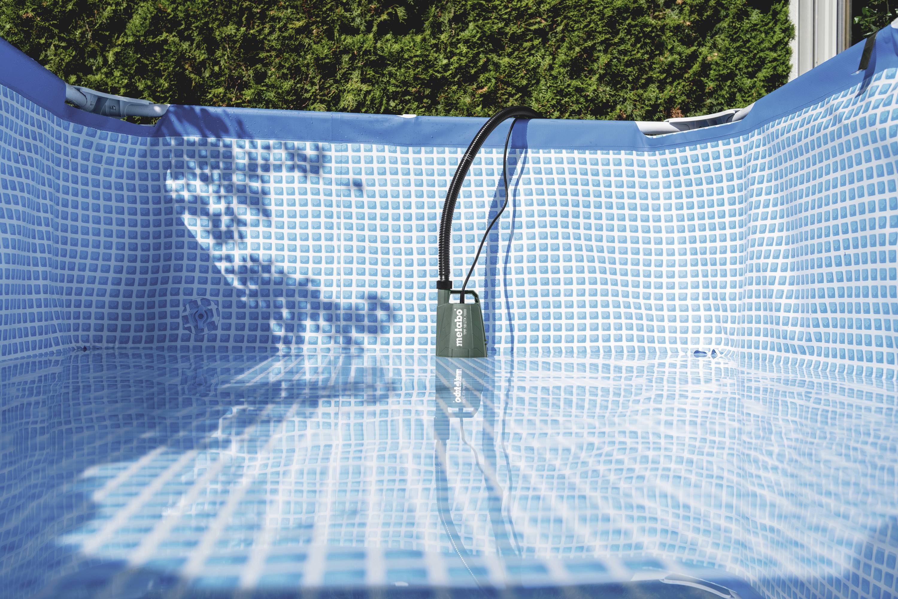 Inflatable pool with low water level and water pump in the centre, surrounded by hedges in the background.