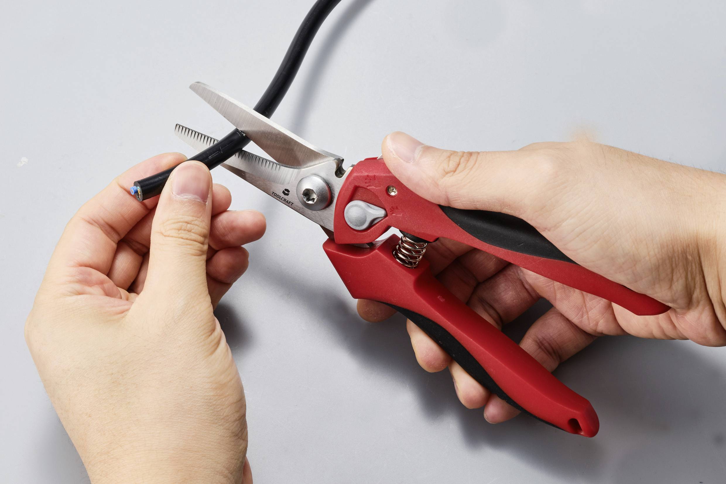 A person is cutting a black cable with red wire cutters.