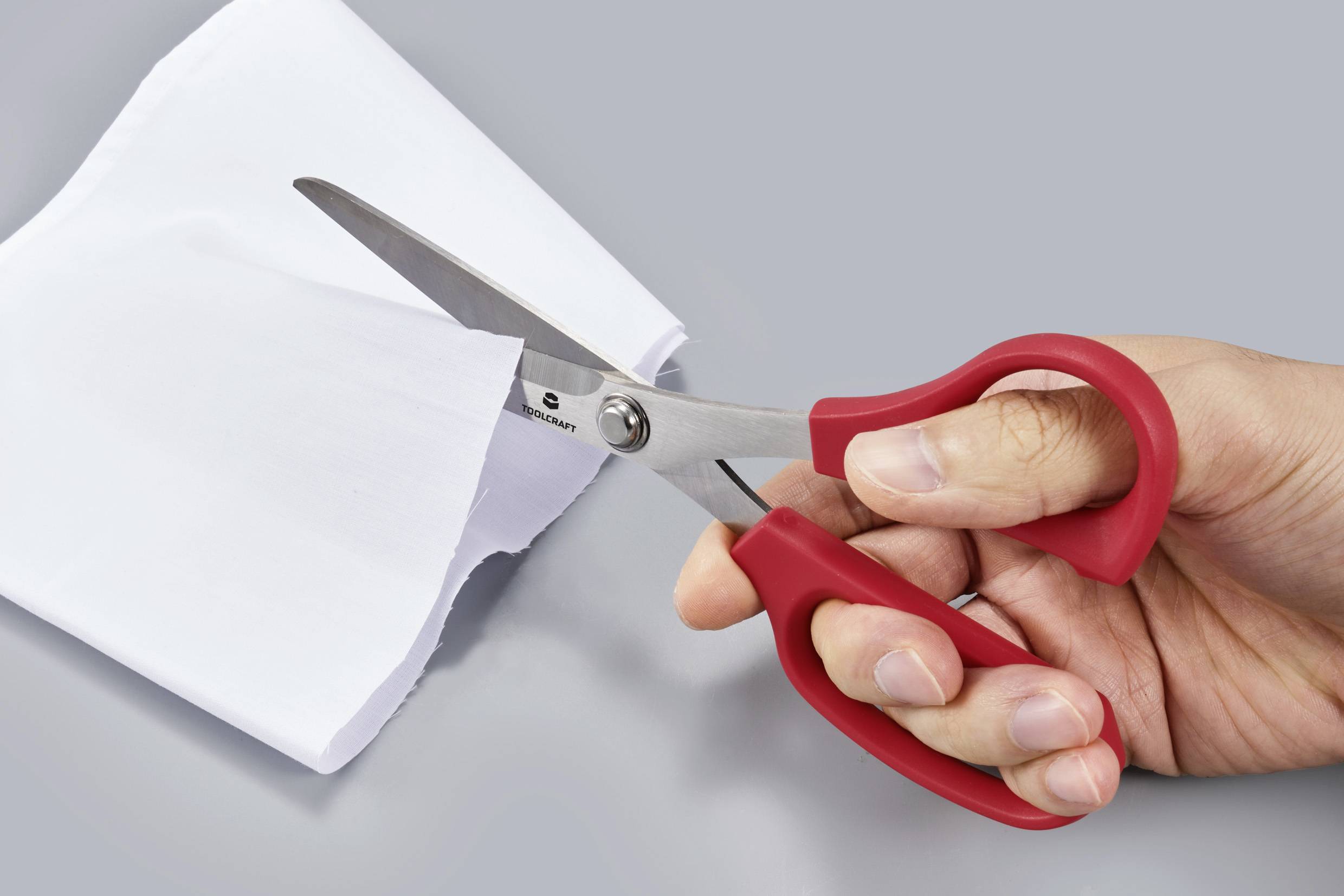 A hand is holding a red pair of scissors and cutting white paper.
