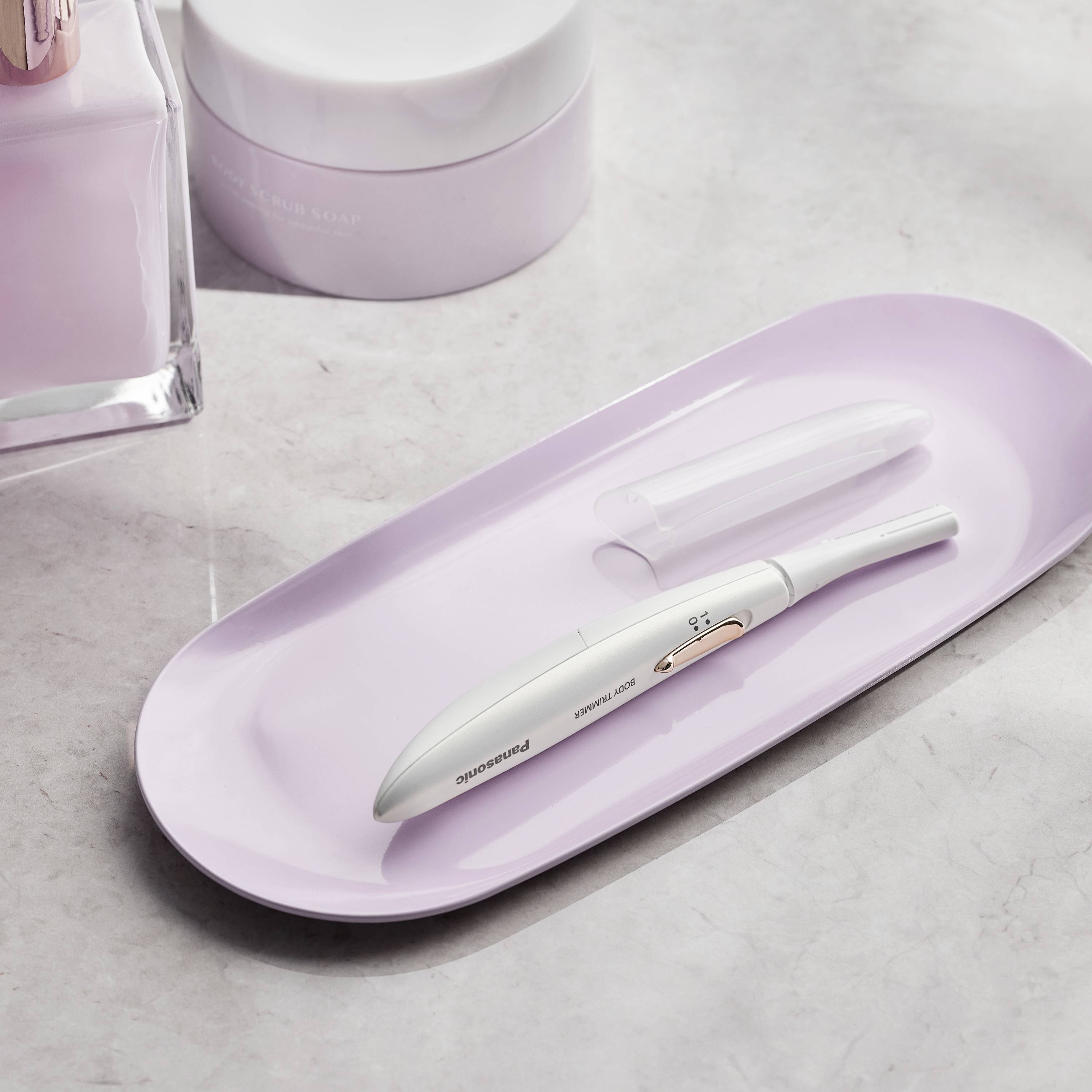 An electronic nail care device and two cream jars on a pink tray on a marble surface.