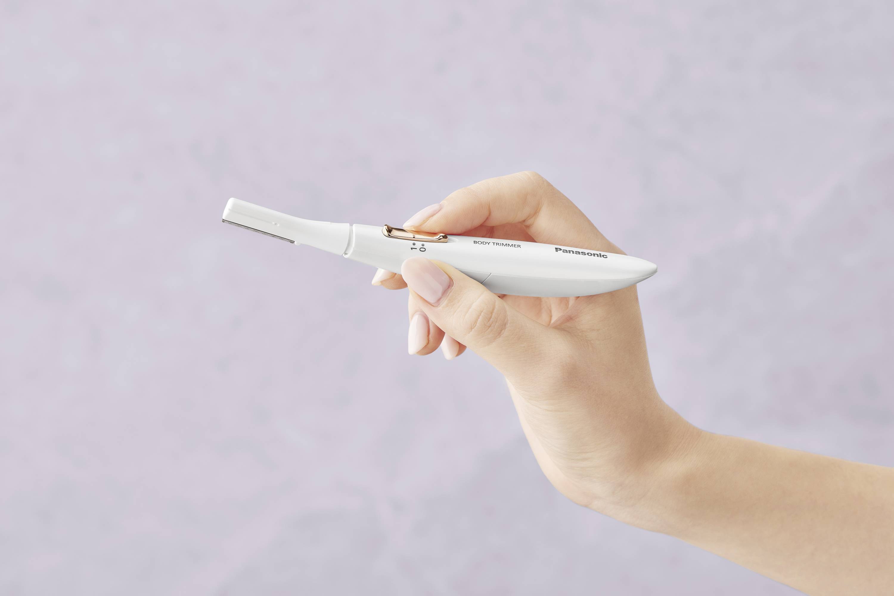 A hand is holding a small, white electric razor against a pastel-coloured background. The razor appears compact and easy to handle.