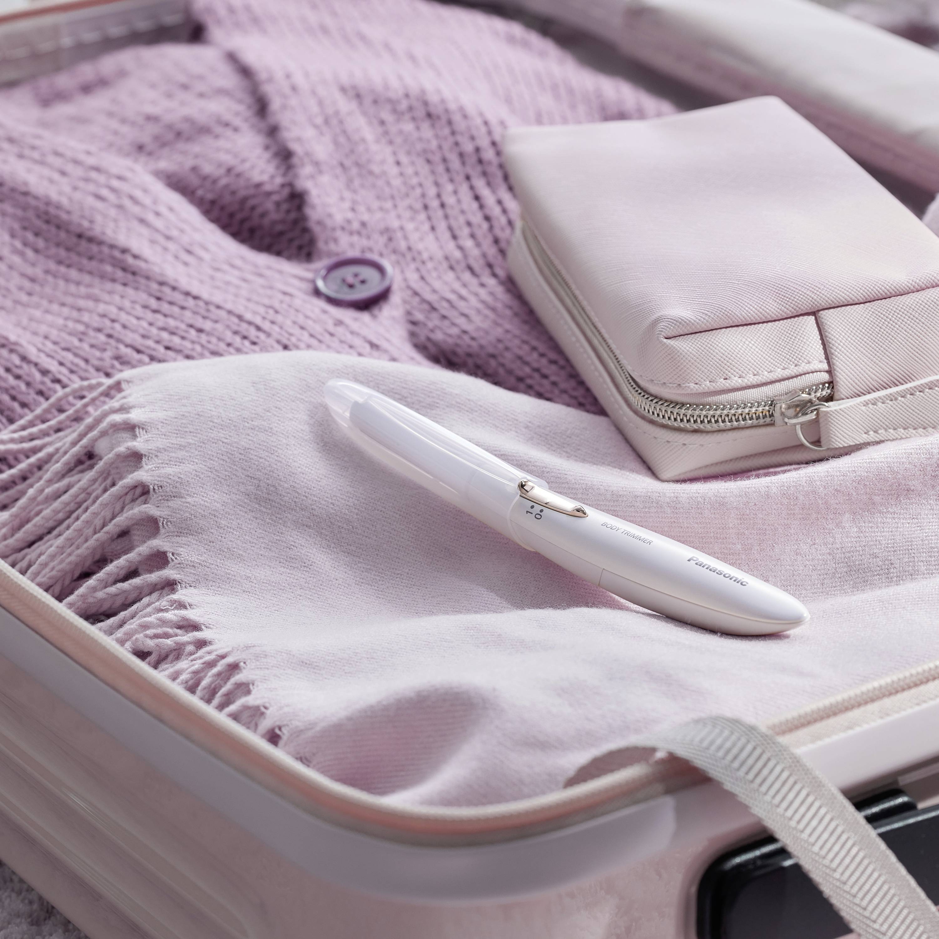 An open suitcase reveals a folded pink cardigan and a pink purse. A pink toothbrush is placed on top.