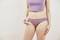 A woman wearing a purple top and underwear is holding a sanitary liner. The background is neutral. Topic: Intimate hygiene.