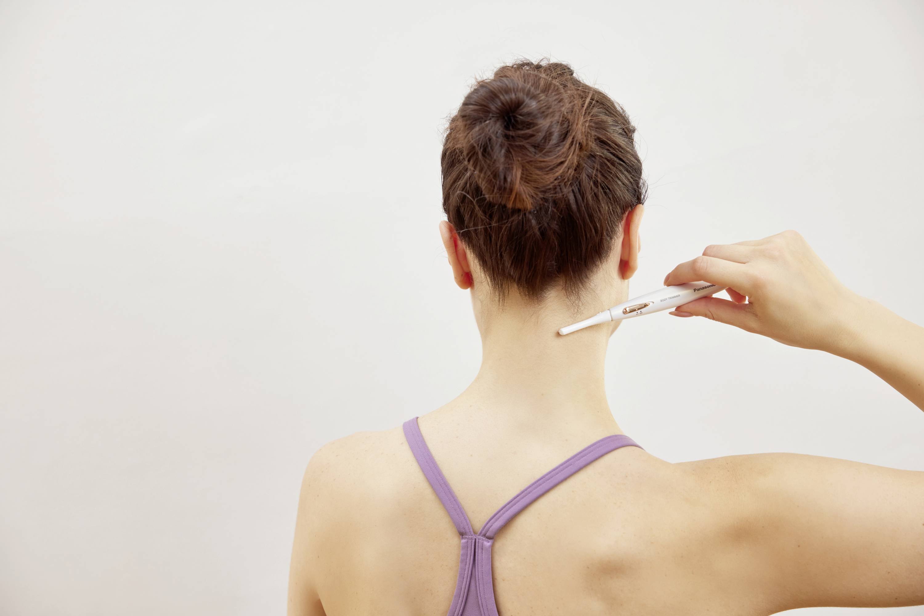 A person is pointing to their neck with a white pen. They are wearing a purple top. The background is grey and neutral.