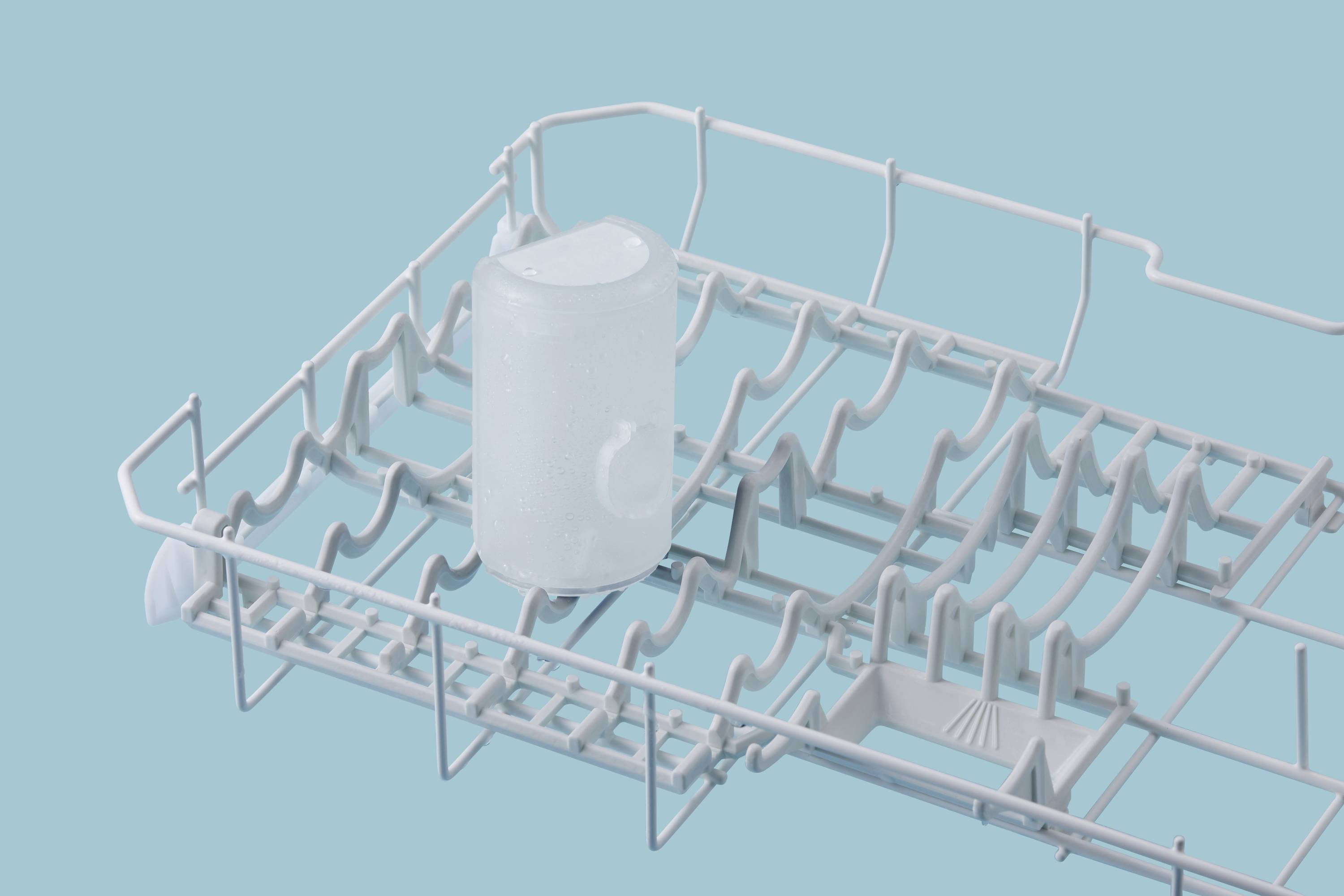 An empty dishwasher rack with an upturned clear glass in the centre, set against a teal background.