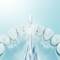 A toothbrush sprays water in a high-speed capture to remove plaque from white teeth, against a light blue background.