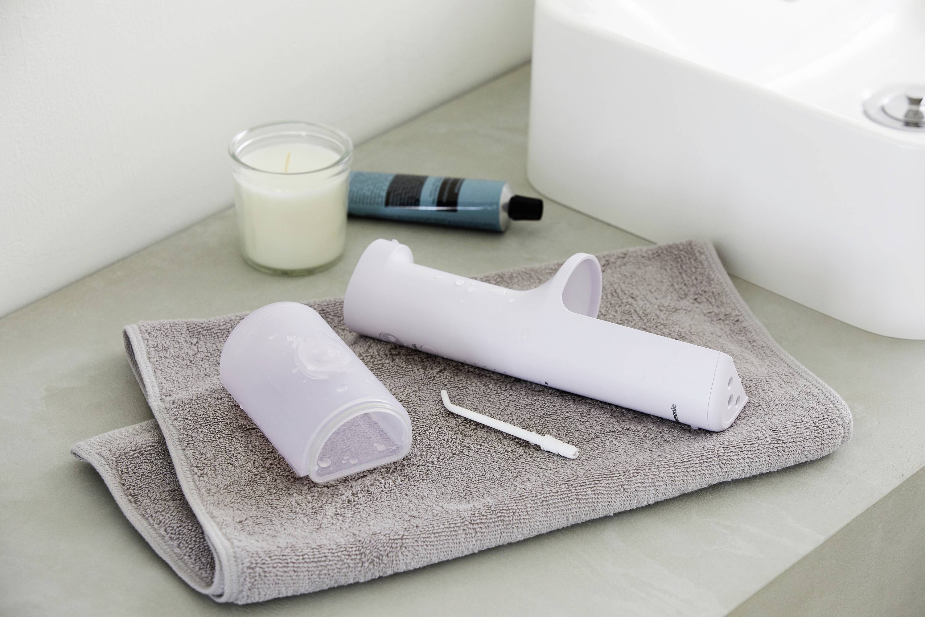 Dental hygiene items laid out on a grey towel beside a candle and toothpaste on a washbasin.