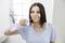 A woman uses a water flosser for tooth cleaning in a bright bathroom. She is wearing a light blue T-shirt and smiling.