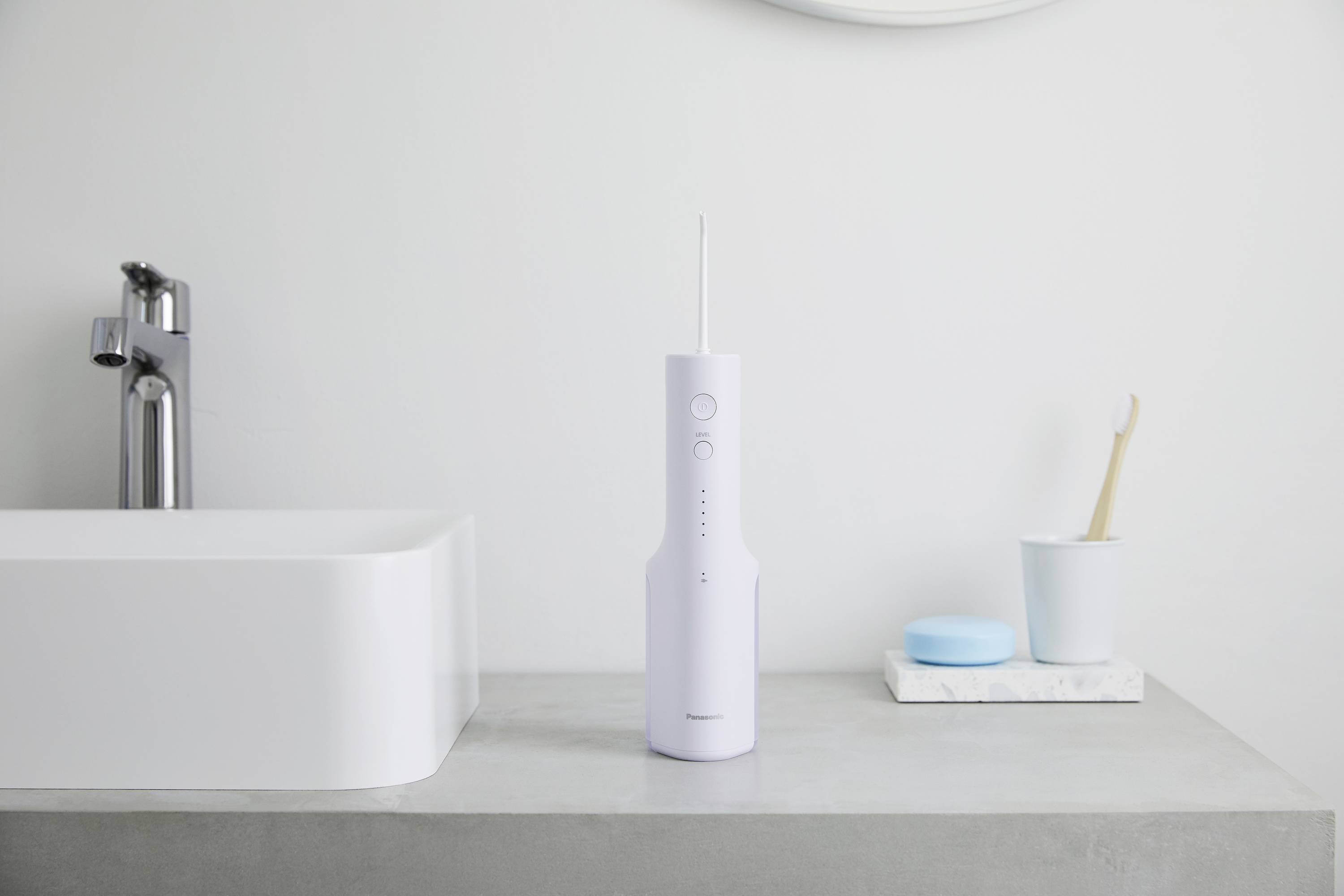 Electric water flosser on a bathroom sink edge beside a toothbrush and tap, minimally designed.