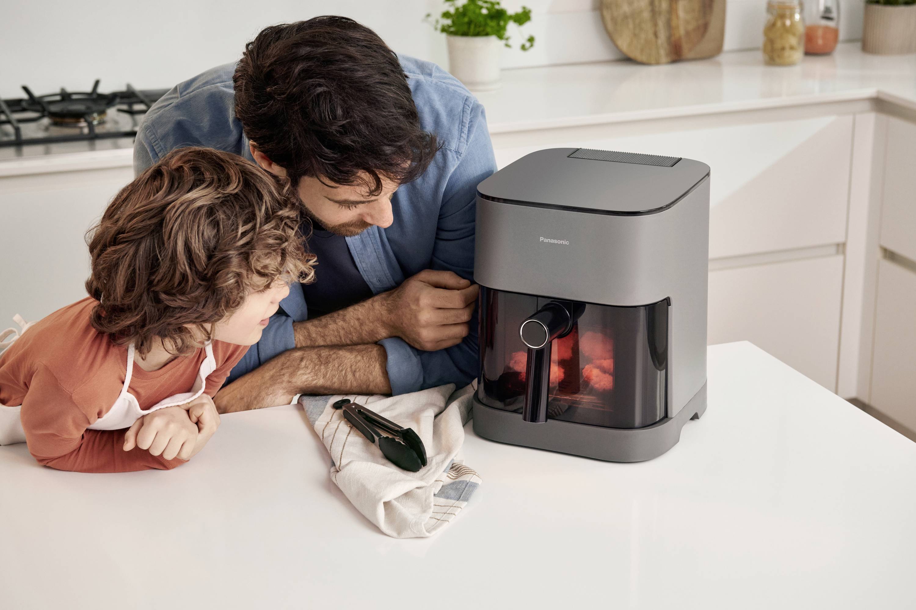 A man and a child are observing a modern air fryer together in a bright kitchen.