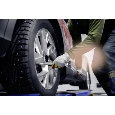 A mechanic is changing a car tyre in a garage. The vehicle is jacked up, and the mechanic is using a spanner.