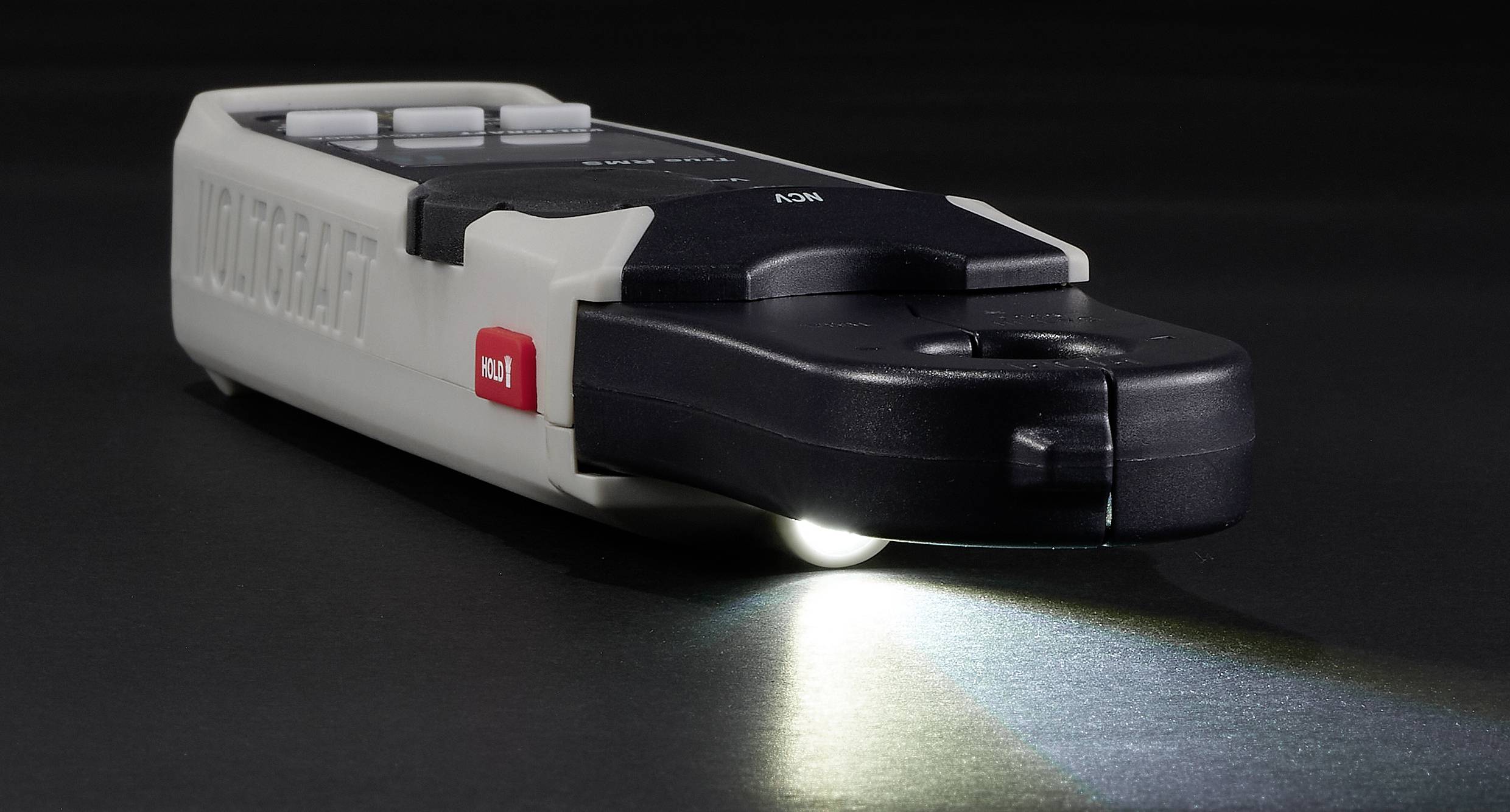 A flat, black LED torch on a table, with its light switched on. A red button is visible on the side.