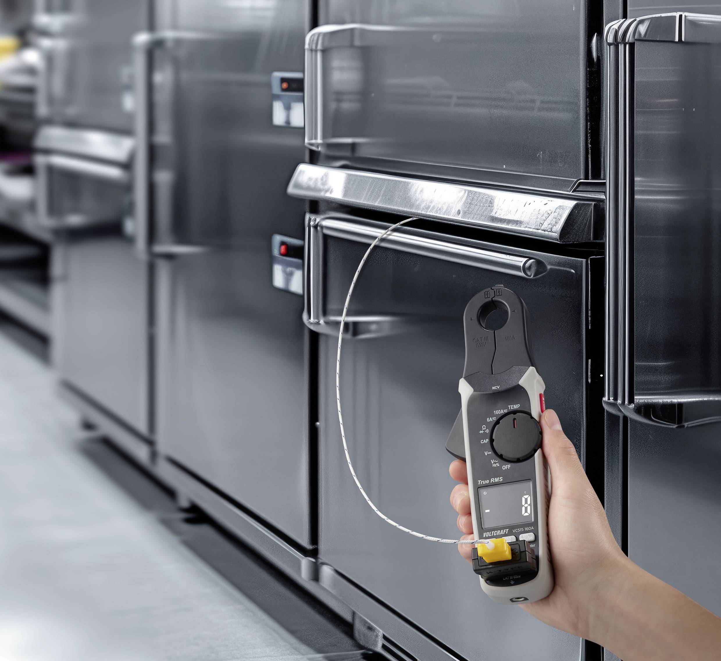 A person is holding a digital measuring device in the foreground, with kitchen appliances in the background. The measuring device is displaying a value of 0.