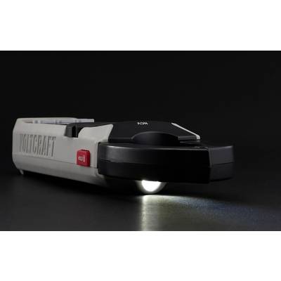 A grey Voltcraft voltmeter on a dark background, with an illuminated torch at the bottom edge.