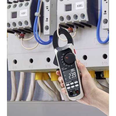 A hand is holding a digital electricity meter with clamp function in front of an electrical cabinet, displaying a measurement of 239 volts.