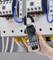 A hand is holding a digital electricity meter with clamp function in front of an electrical cabinet, displaying a measurement of 239 volts.