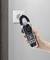 A hand holds a multimeter up to a socket on the wall. The multimeter displays electrical measurement readings.