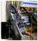 Gloved technician uses a clamp meter on electrical wiring in a panel; smartphone app displays voltage and waveform readings.