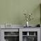 A grey piece of furniture against a green wall, with a vase of dried flowers and a digital calendar placed on top.