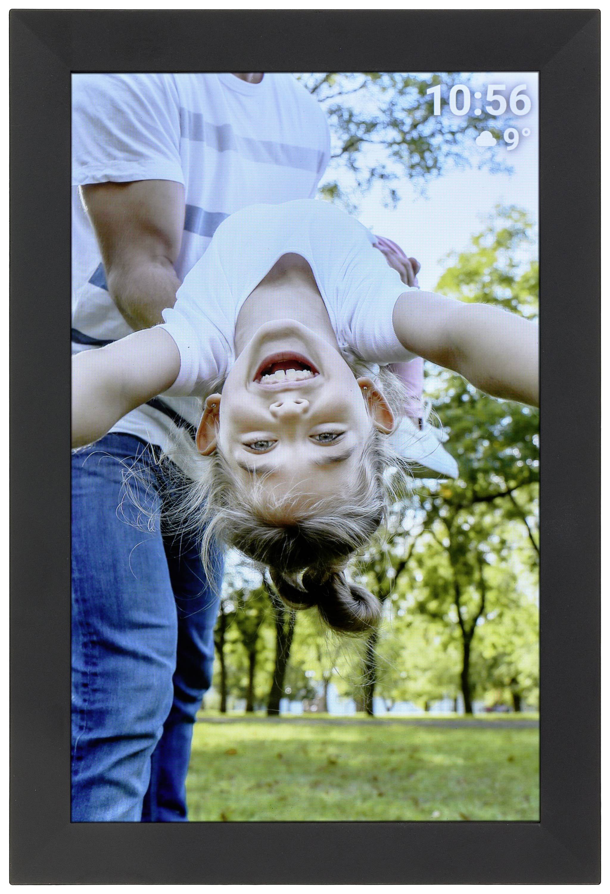 A man is holding a laughing child upside down in a park. It is sunny, with trees in the background. Time is 10:56, temperature 9 degrees.