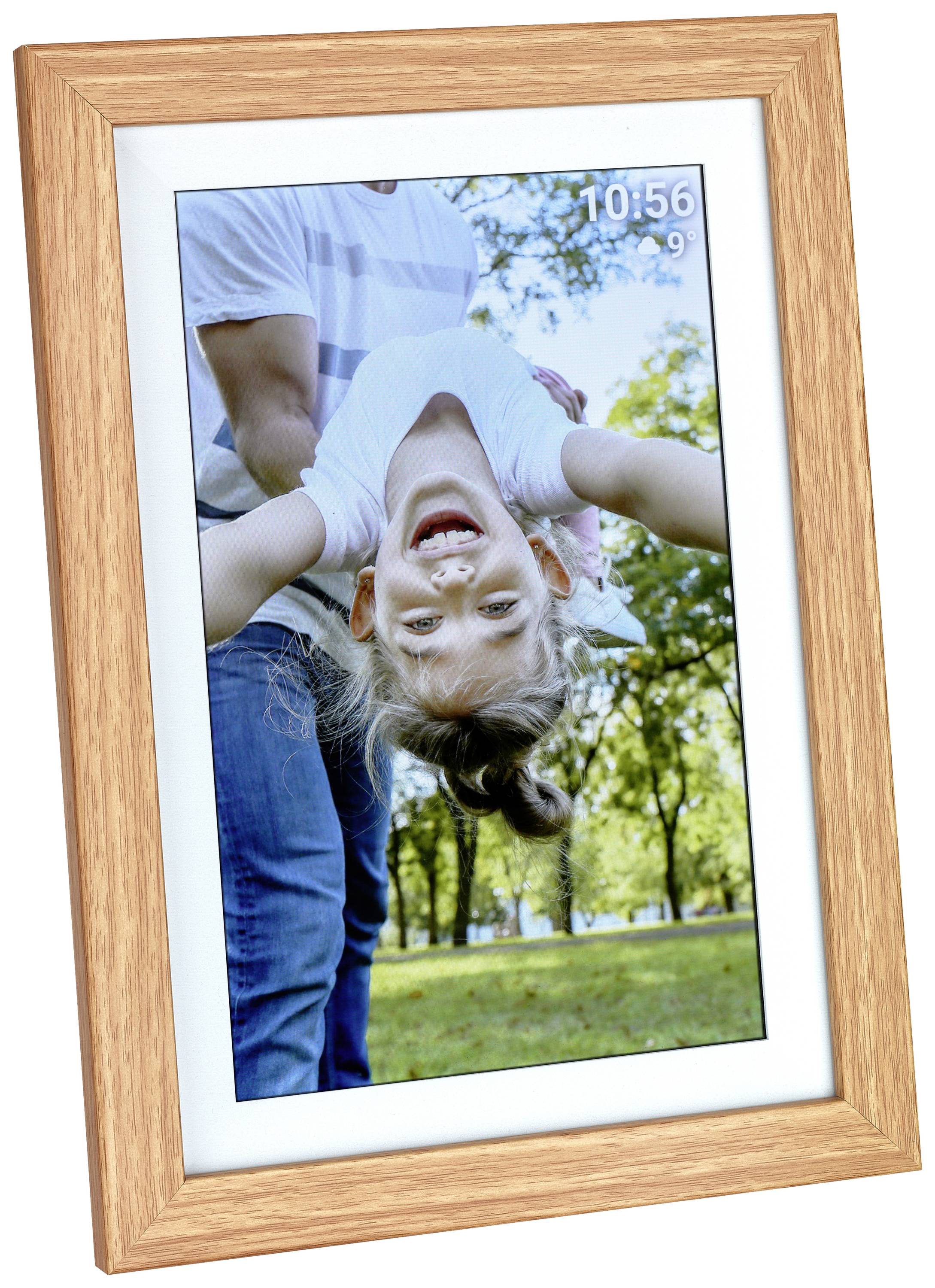 A smiling girl is hanging cheerfully upside down in a park, held by an adult in the background.