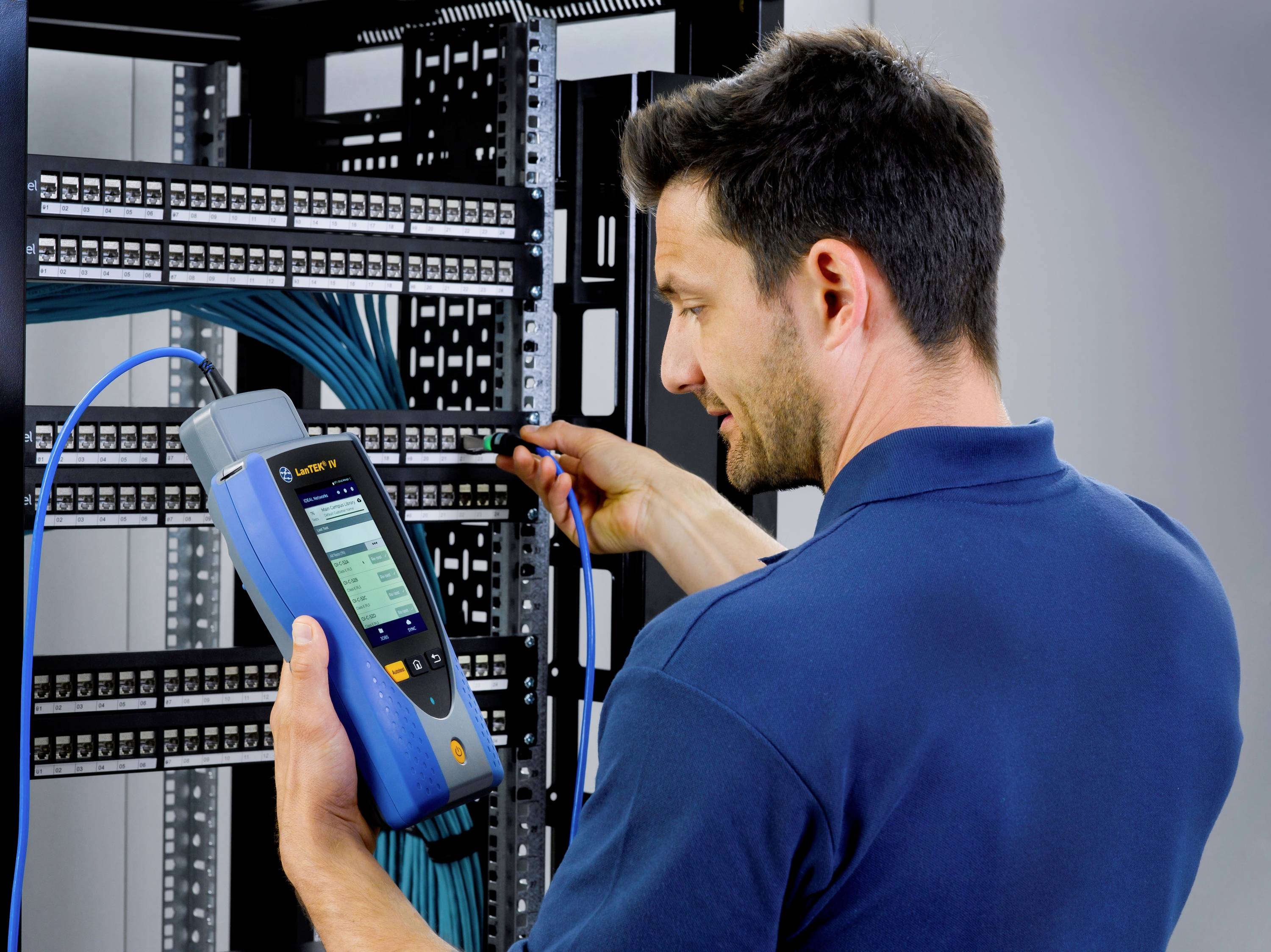 A technician in a blue shirt is calibrating a network testing device in a server room to check the network connection.