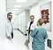 Three medical professionals are chatting in the hospital corridor. A poster on the wall reads: 'Be a hero, donate blood'.