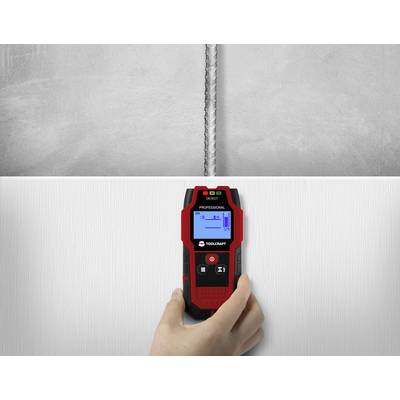 A person is holding a digital locator against a wall to find metal behind the surface. The display shows a metal signal.